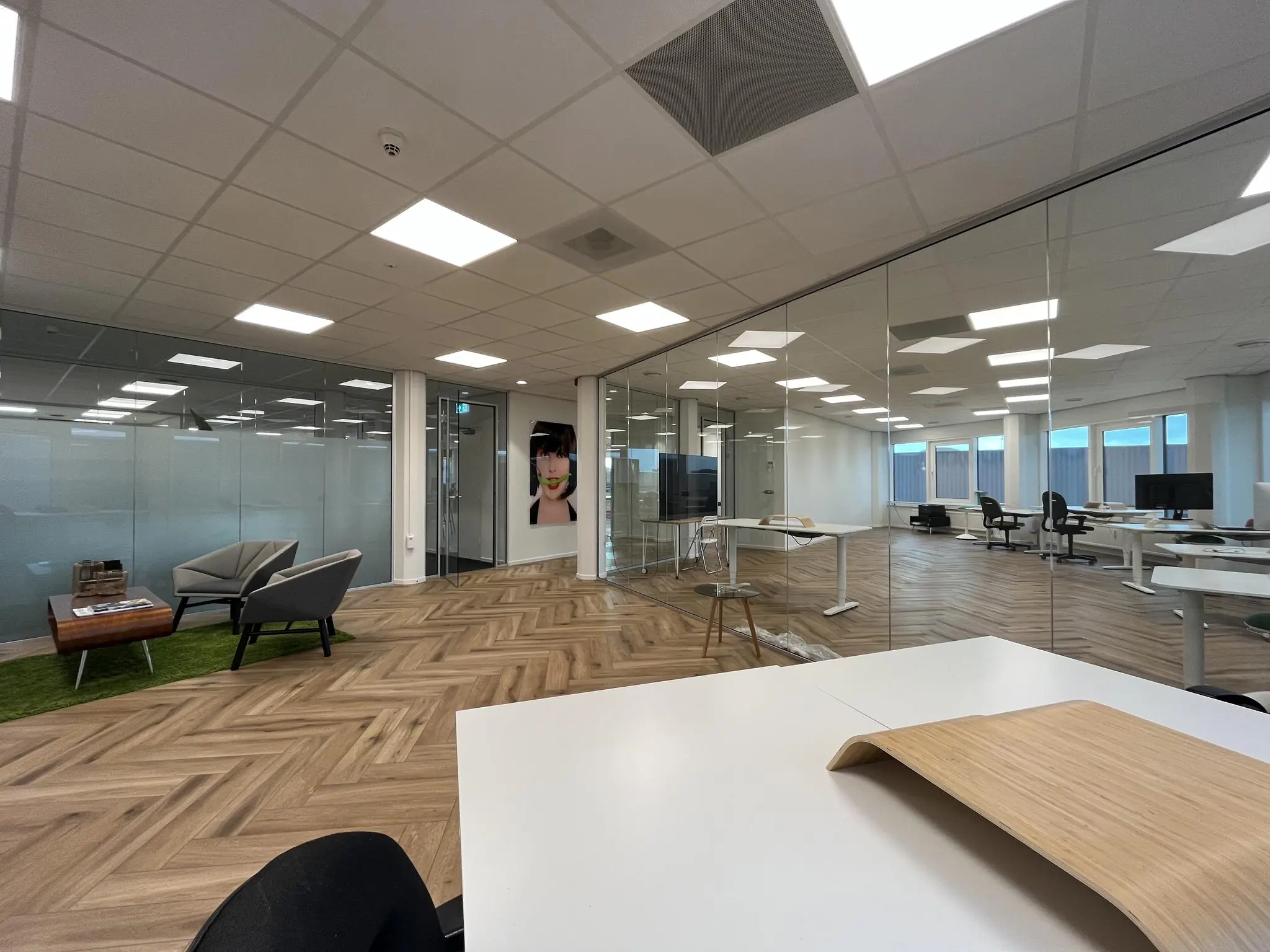 Moderne kantooruimte aan de Lange Dreef met glazen wanden, houten visgraatvloer en minimalistische inrichting.